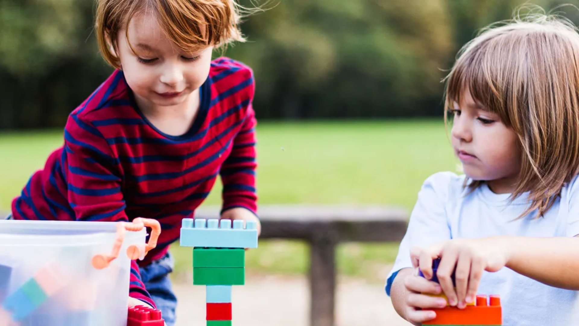 Two children playing with blocks outside.