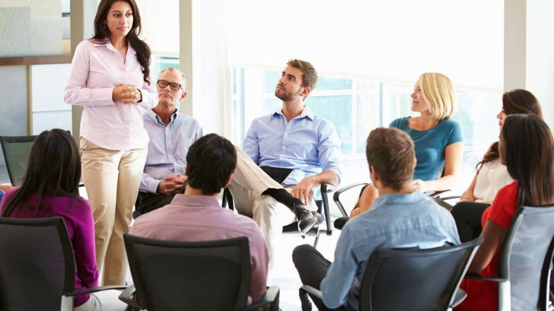 Woman presenting in front of people sitting in a circle.