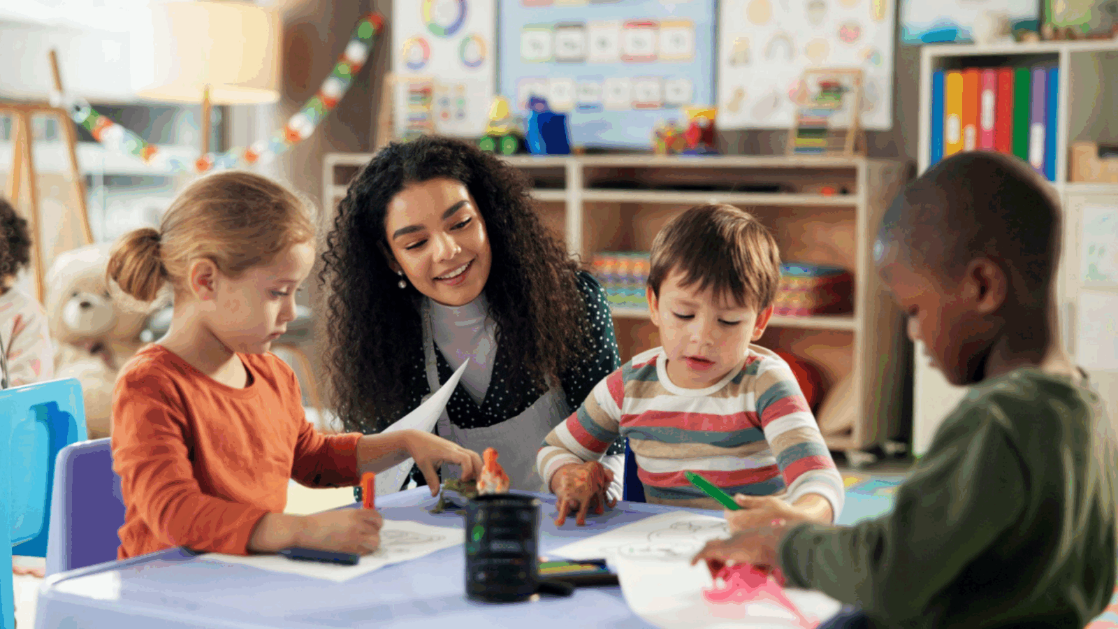 Teacher working with young students at a table inside a classroom.