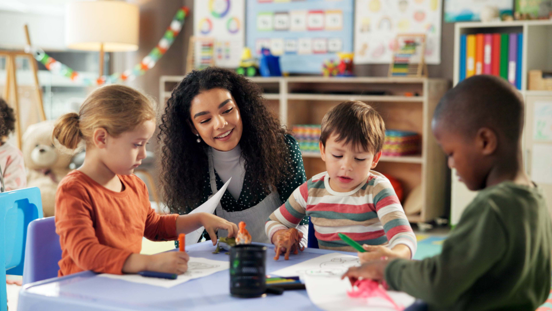 Teacher working with young students at a table inside a classroom.