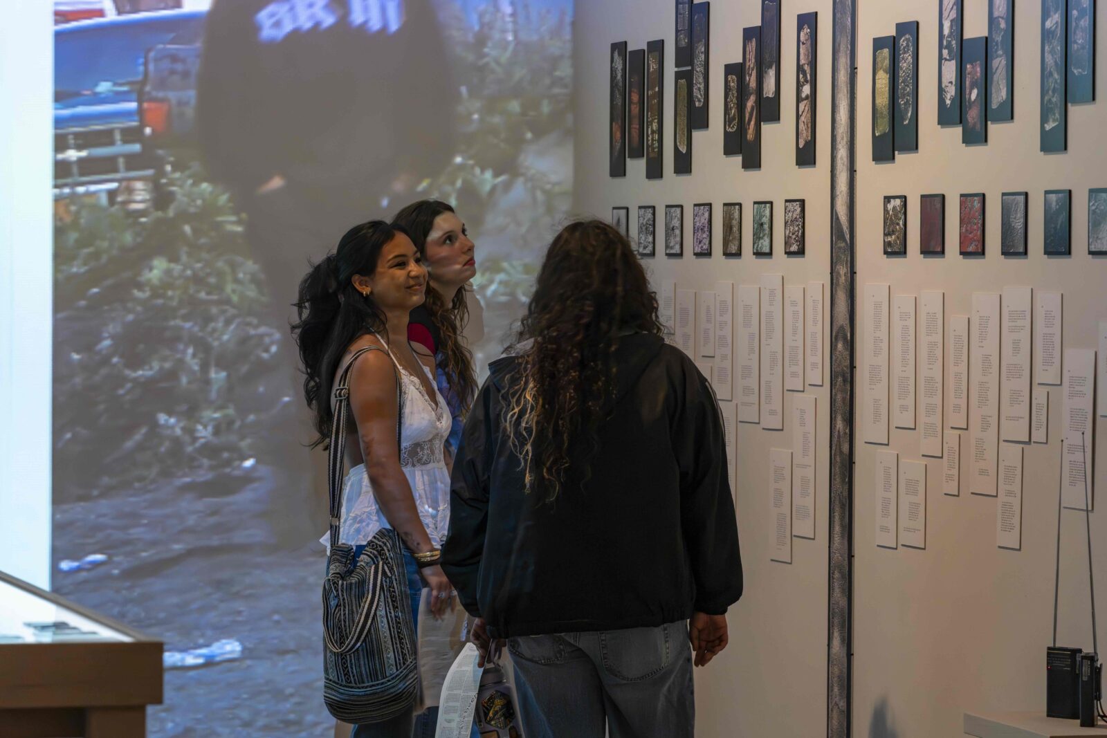 students stand in front of a wall with multiple photographs on it