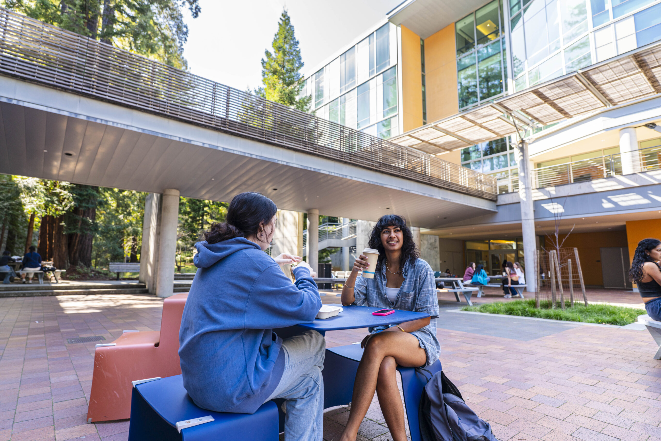 Two students sit in the BE Courtyard and drink coffee