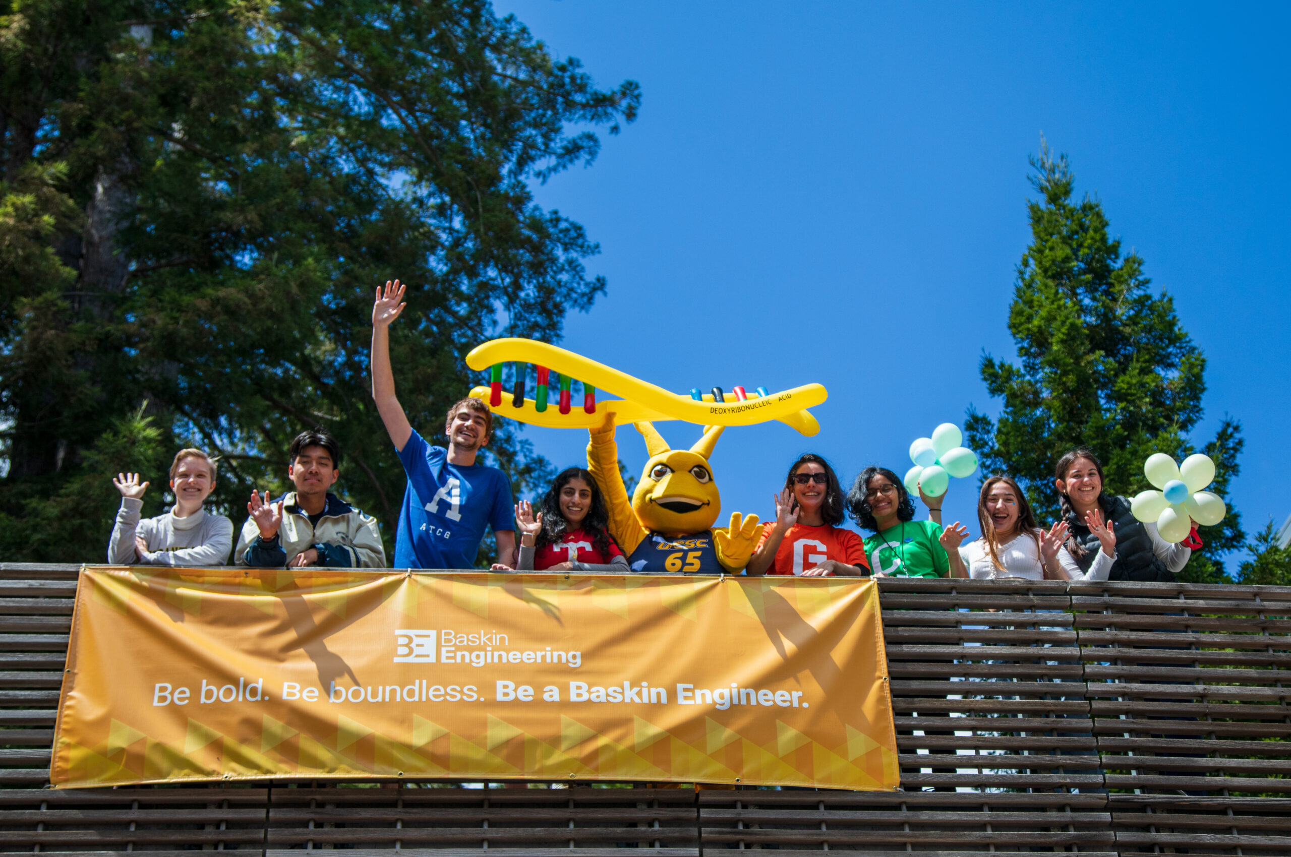 Students standing on a bridge with the sammy slug mascot and a large inflatable DNA double helix model.