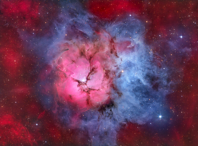 Vivid red and blue nebula with a bright pink central glow, surrounded by wispy dark dust lanes and scattered stars.
