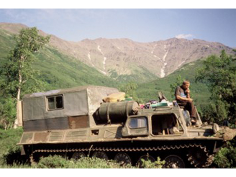 Man sitting on front of armored tank, thinking, in lush tropical mountain