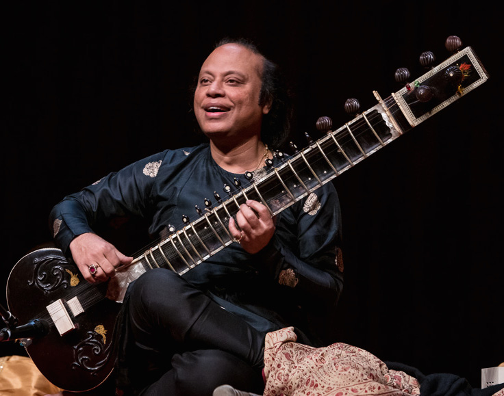Tabla maestro Nishat Khan playing an instrument against a dark background